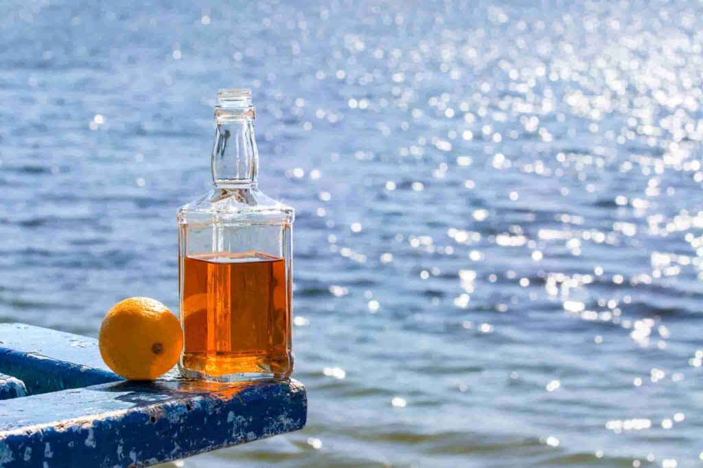 Bottle of whiskey and lemon on the table by lake