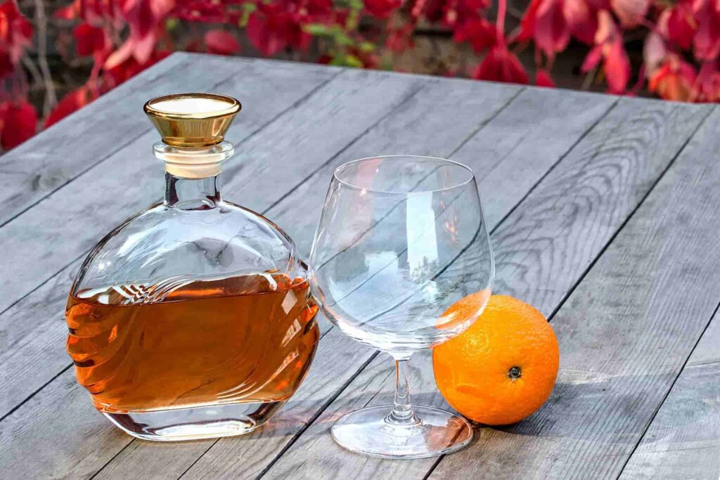 Bottle of brandy and a snifter with orange on the old table in autumn garden's