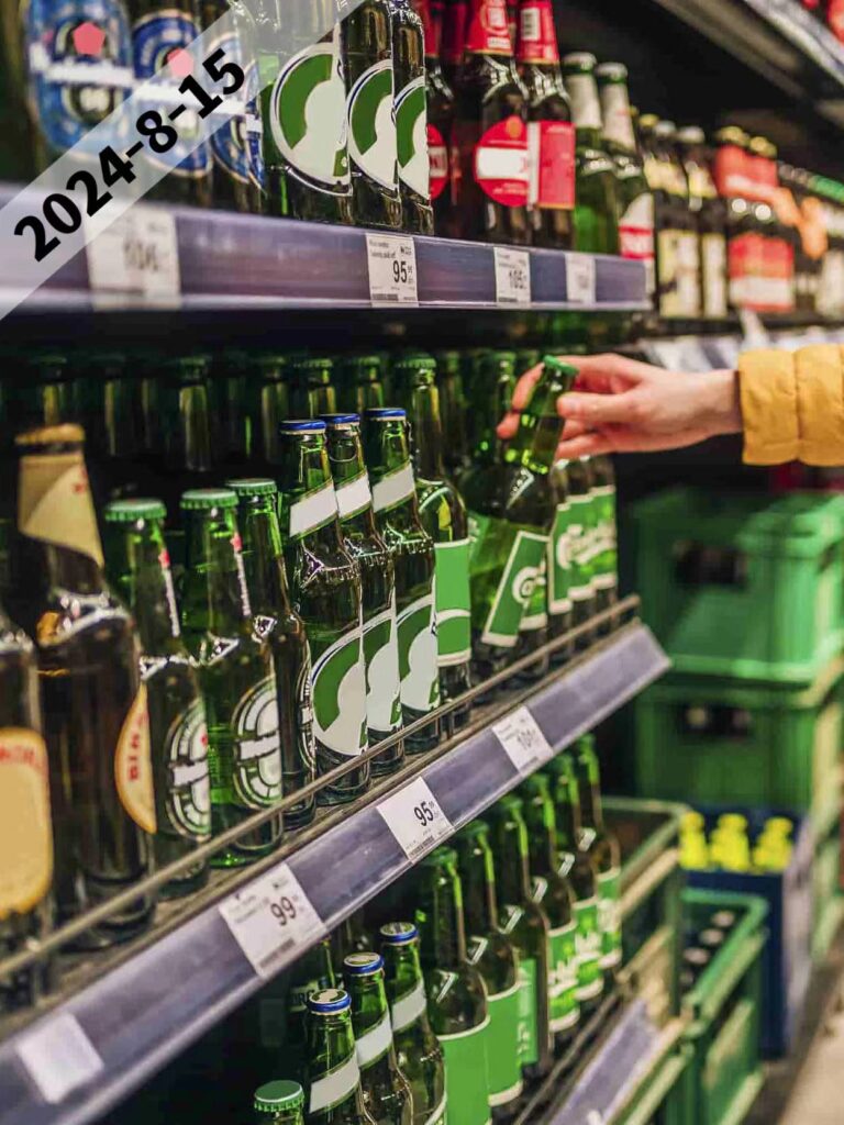 Shopper choosing green glass beer bottles from a supermarket shelf, highlighting brand variety